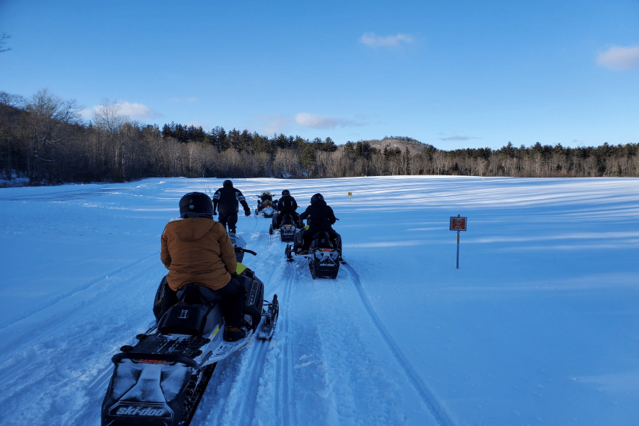 Snowmobilers riding across a snowy trail near Moosehead Lake in Greenville, Maine
