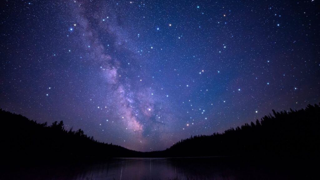 the milky way over a lake with trees