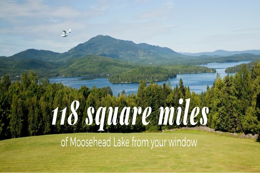 A blue sky, green grass and mountain tower over beautiful Moosehead Lake