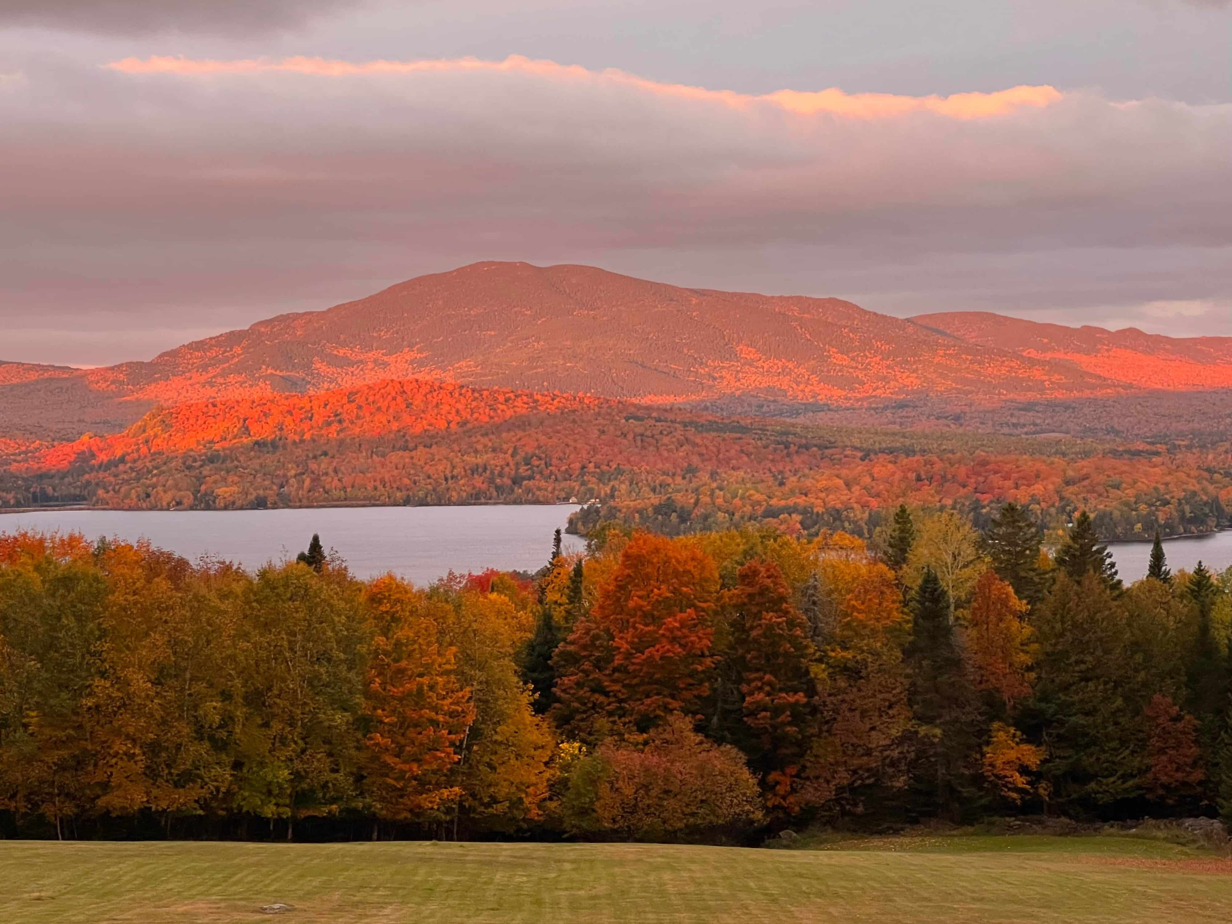 Scenic autumn landscape of a mountain and lake at sunset, with vibrant fall foliage in red, orange, and gold tones