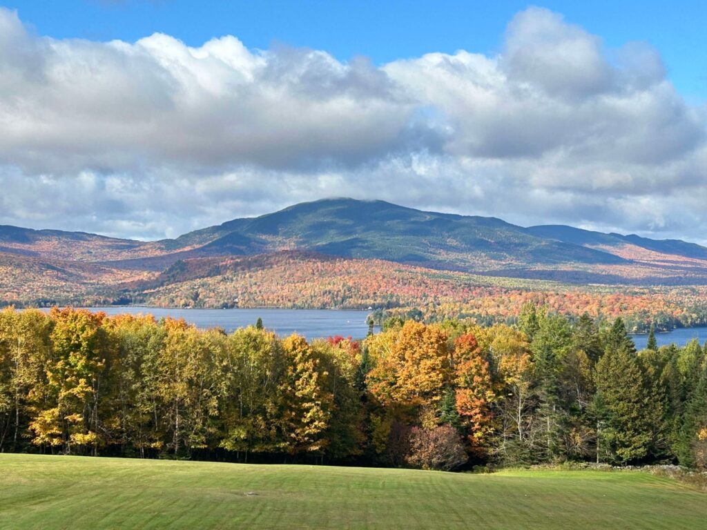 Moosehead Lake in Maine surrounded by colorful fall foliage and mountains under a partly cloudy sky