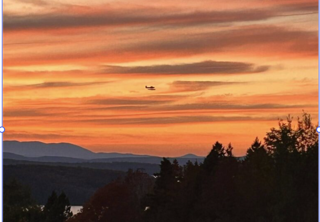 A small floatplane flies through a dramatic Maine sunset above the mountains and forests surrounding Moosehead Lake, capturing the breathtaking aerial adventure offered in Lodge at Moosehead Lake's Land, Lake & Air package